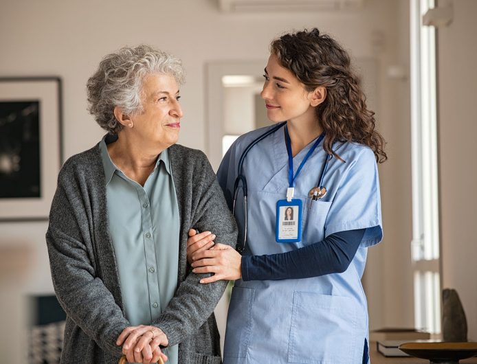 Young caregiver helping senior woman walking. Nurse assisting her old woman patient at nursing home. Senior woman with walking stick being helped by nurse at home.